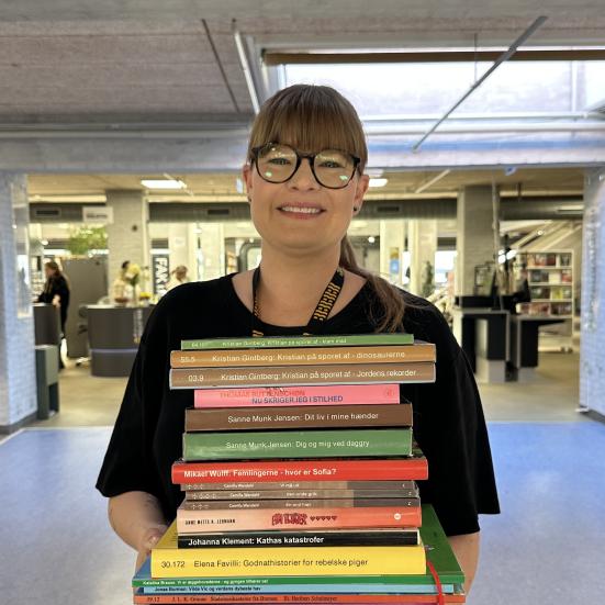 Bibliotekar står på biblioteket med en bunke bøger for hele familien