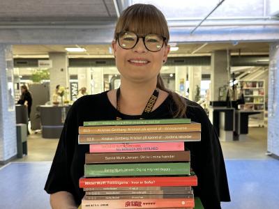 Bibliotekar står på biblioteket med en bunke bøger for hele familien