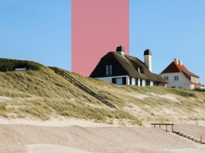 Sommerhuse ligger bag klitter ved en sandstrand under blå himmel.