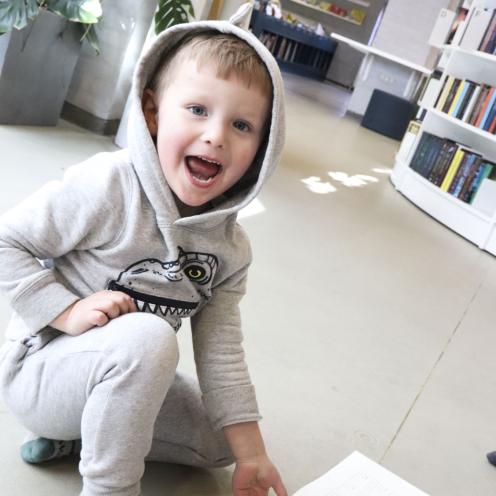 Billede af glad dreng med bog på gulvet i børnebiblioteket