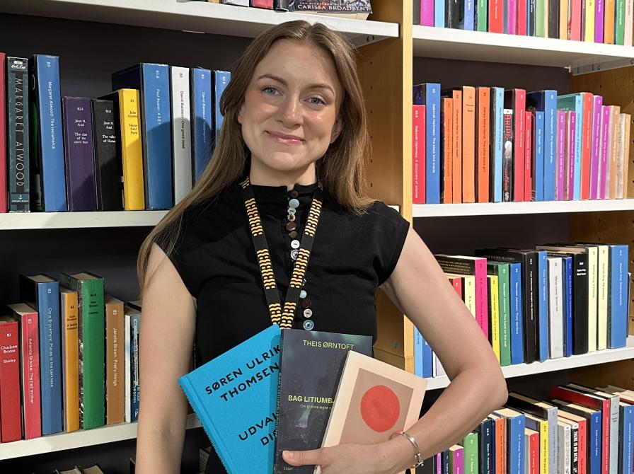 Bibliotekar står i biblioteket og holder tre bøger